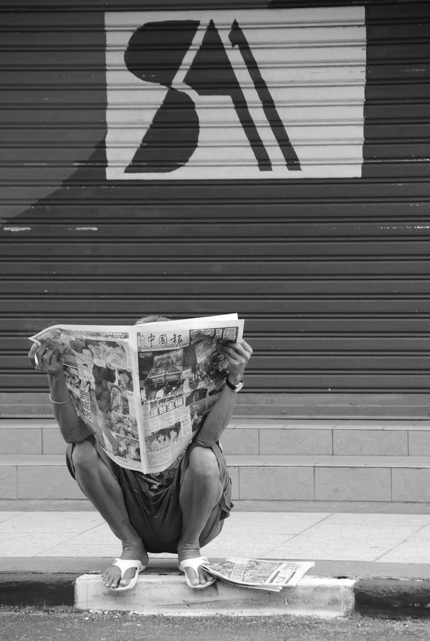 person sitting on side walk reading newspaper