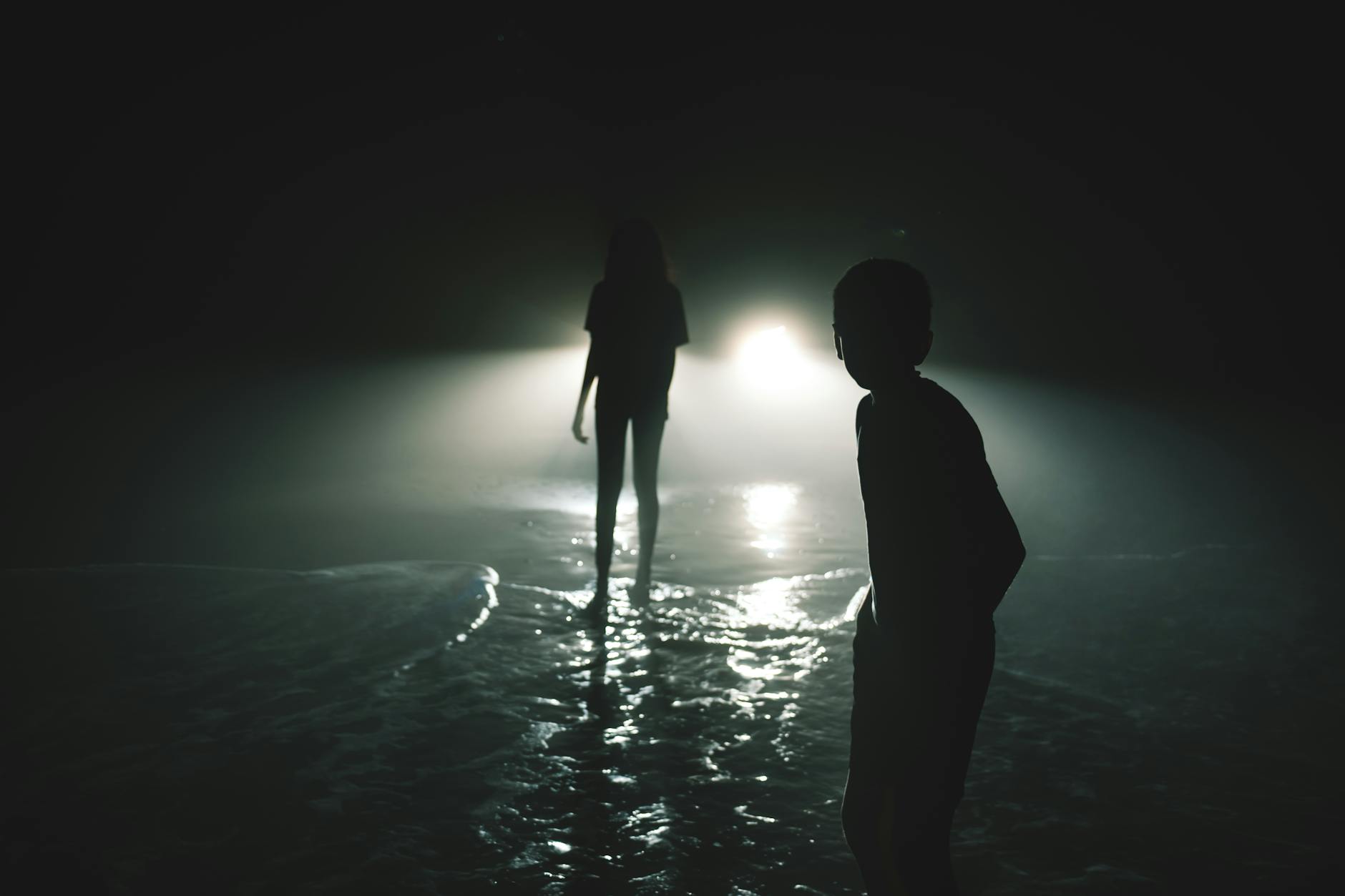 silhouettes of two people standing on the background of car lights at night