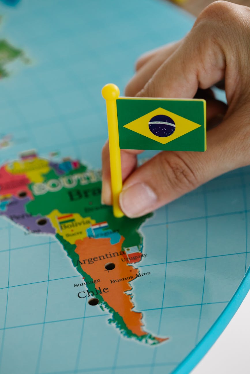 person holding a mini brazil flag pinned on a map